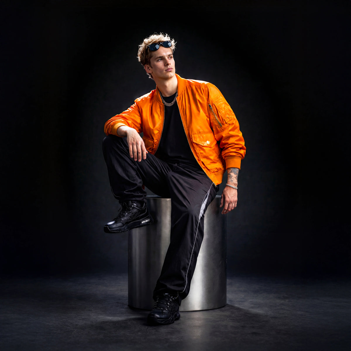 Person wearing an orange jacket sitting on a metallic stool against a black background
