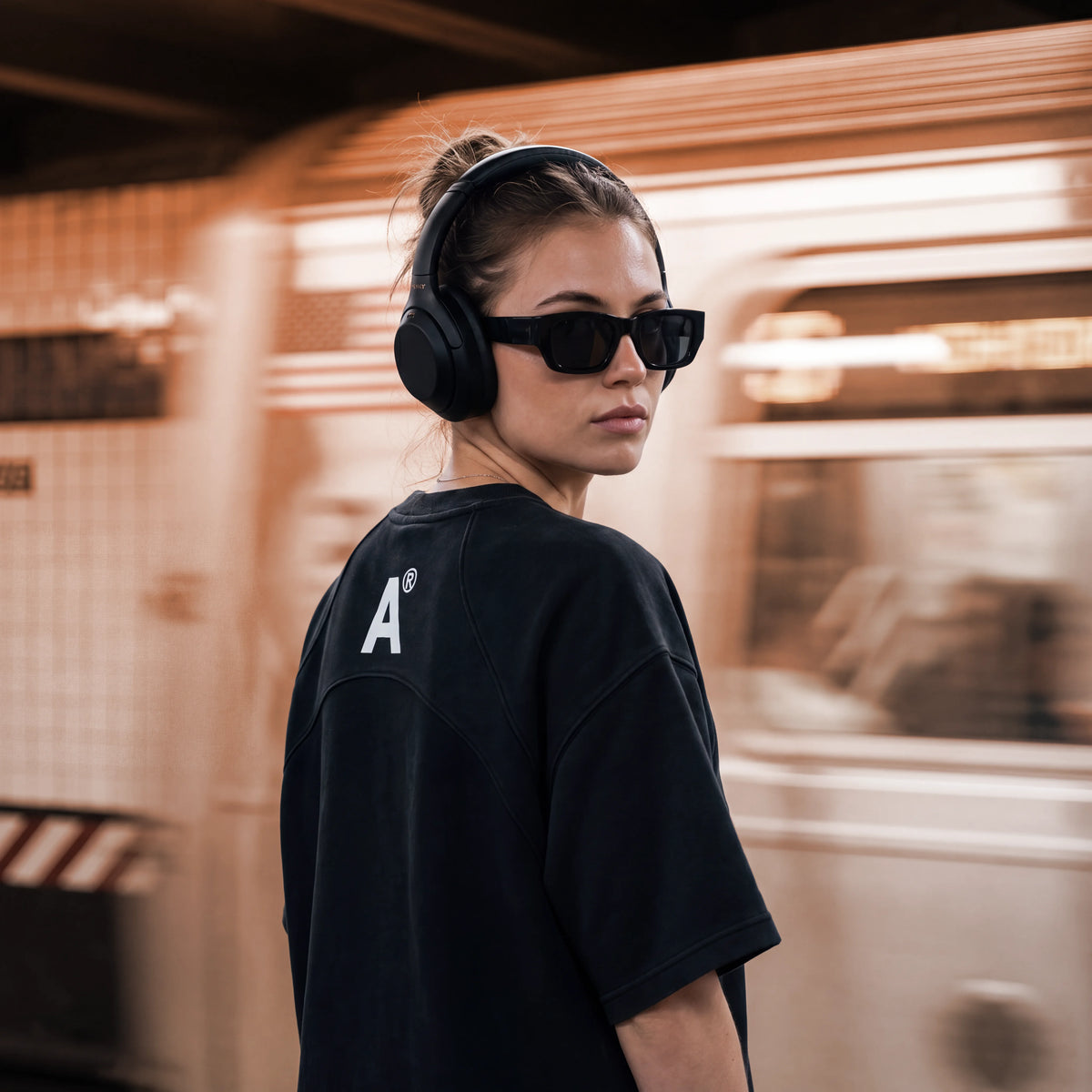 Person wearing headphones and sunglasses with a blurred train in the background