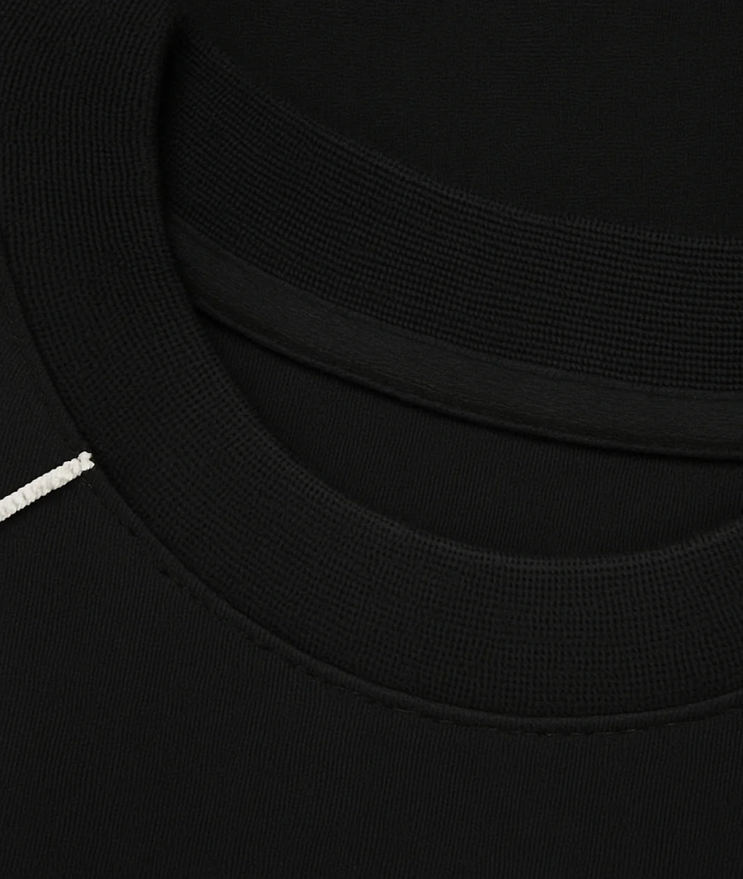Close-up detail of a black crewneck sweatshirt showing the ribbed collar, inner neckband, and a small white embroidered accent on the left side.