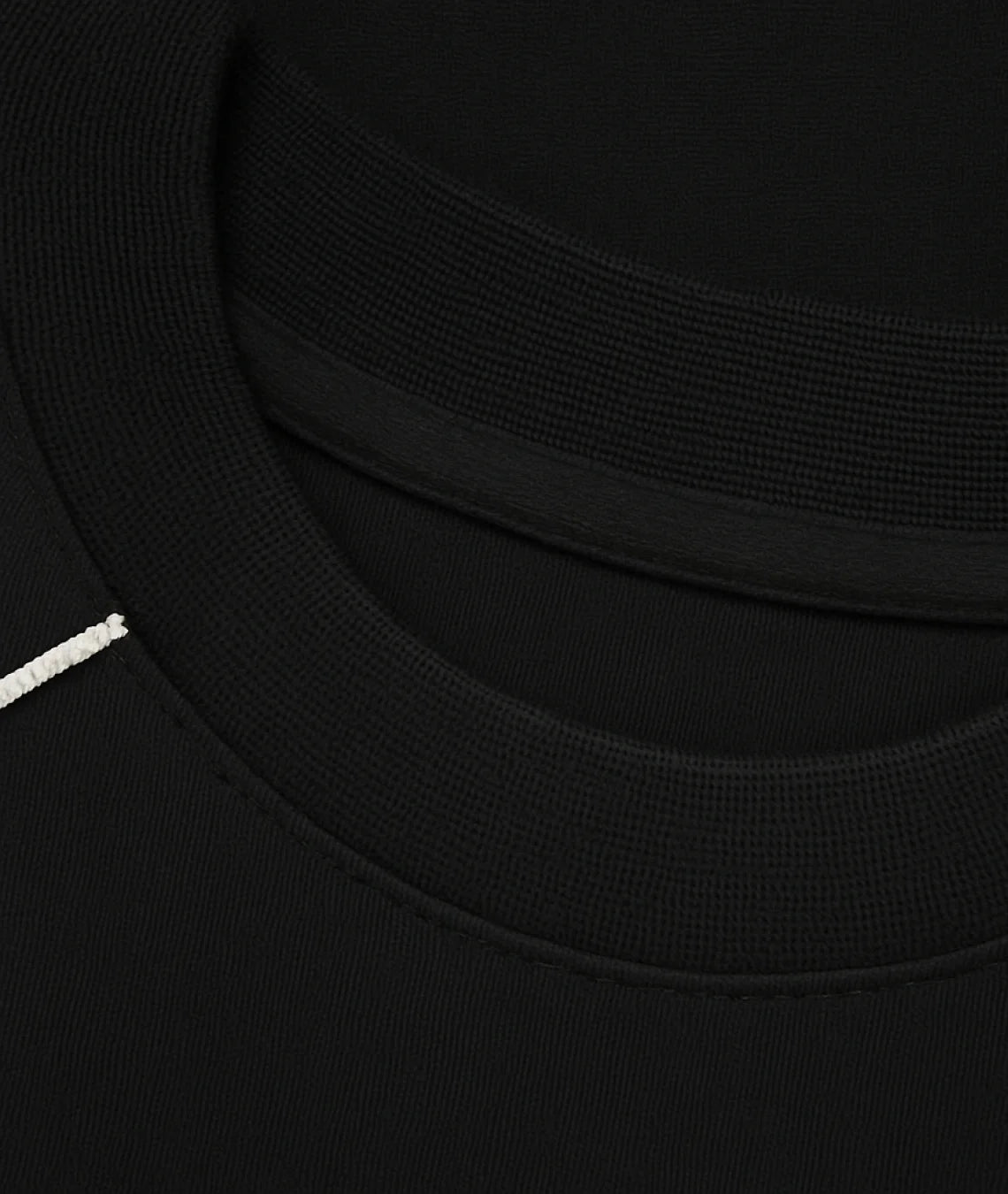 Close-up detail of a black crewneck sweatshirt showing the ribbed collar, inner neckband, and a small white embroidered accent on the left side.