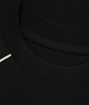 Close-up detail of a black crewneck sweatshirt showing the ribbed collar, inner neckband, and a small white embroidered accent on the left side.