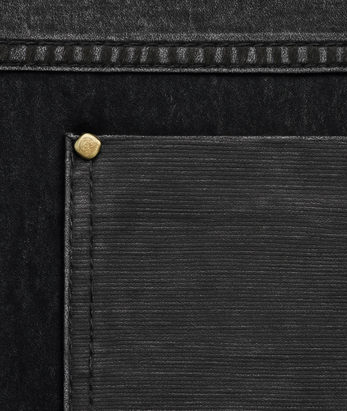 Close-up of a black leather product with a gold rivet detail