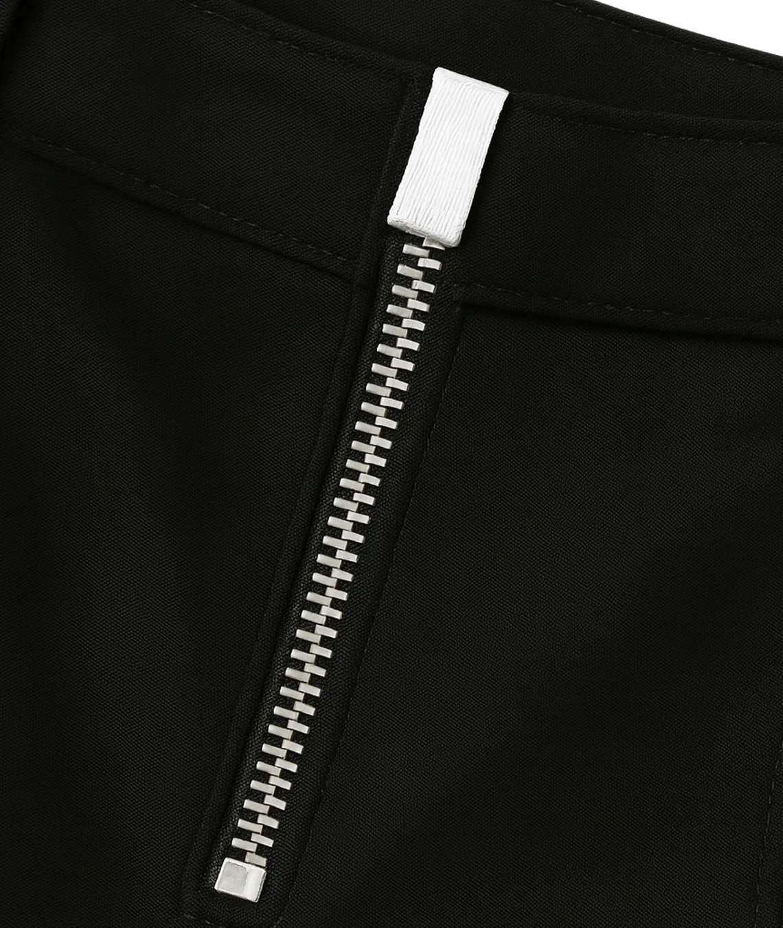 Close-up detail of a black garment featuring a prominent silver zipper with a white pull tab.