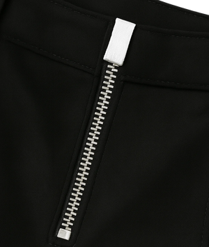 Close-up detail of a black garment featuring a prominent silver zipper with a white pull tab.