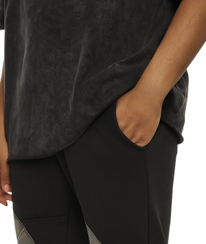 Person wearing a dark gray t-shirt and pants with one hand in a pocket on a white background