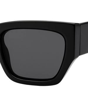 Close-up of a black oversized square sunglasses frame with dark gray lenses on a white background.