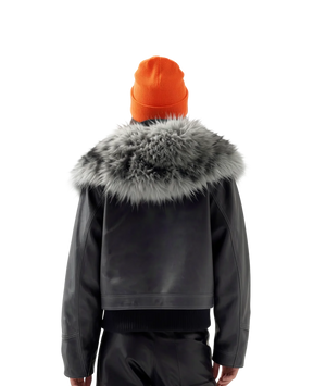 Person wearing a dark jacket with a fur-lined hood and an orange beanie on a white background