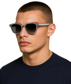 A close-up of a man wearing square sunglasses with a translucent gray frame and dark lenses, paired with a dark navy t-shirt against a solid white background.