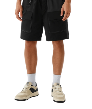 Person wearing black cargo shorts and beige sneakers on a white background