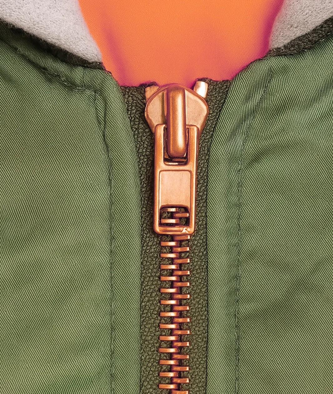 Close-up of a green jacket with a bronze zipper and orange lining.