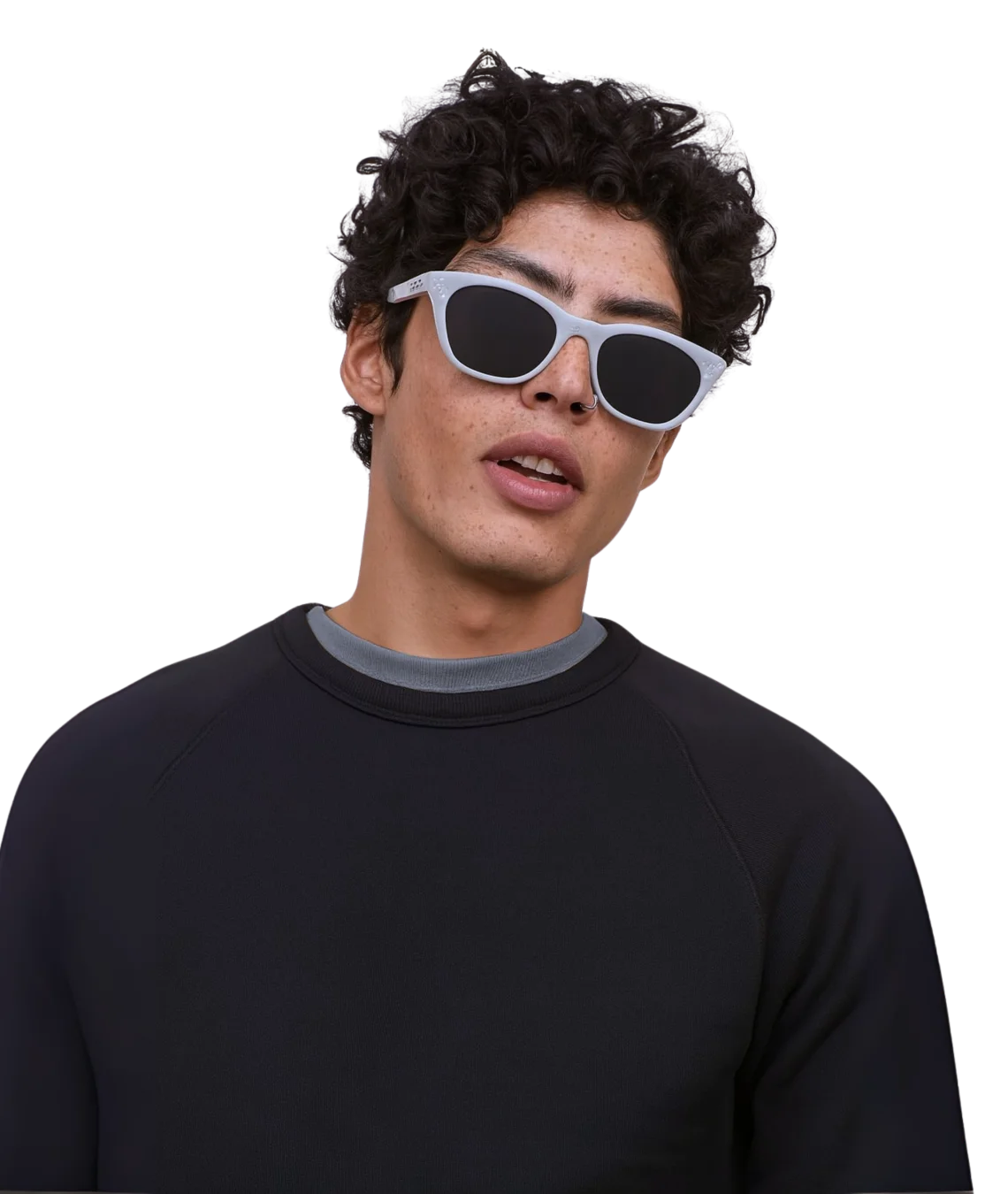A man with curly dark hair wearing white cat-eye sunglasses with dark lenses and a black raglan sweatshirt with a gray crew neck, set against a solid white background.
