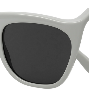 Close-up of a pair of sunglasses with a thick, glossy off-white frame and dark gray lenses, shown against a plain white background.