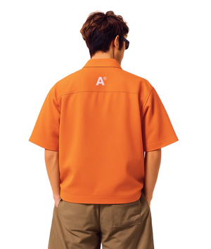 Person wearing an orange shirt with a logo on the back, standing against a white background