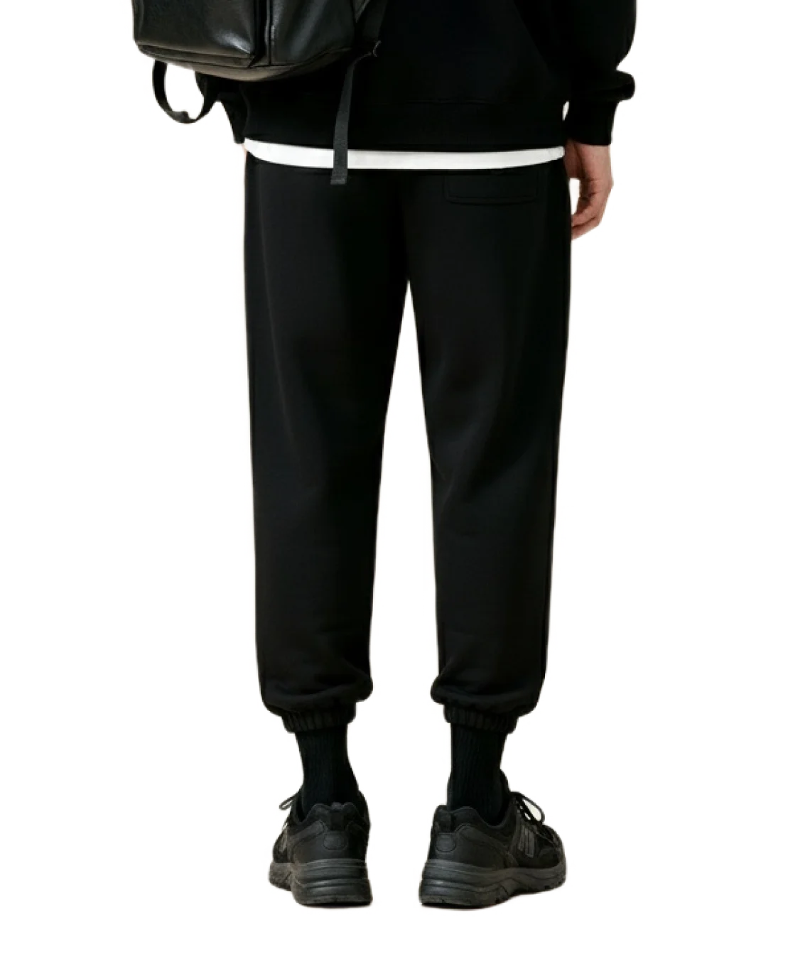 Person wearing black jogger pants and a black backpack on a white background
