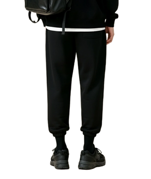 Person wearing black jogger pants and a black backpack on a white background