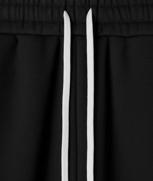 Close-up of black drawstring pants with two contrasting white drawstrings at the elastic waistband.