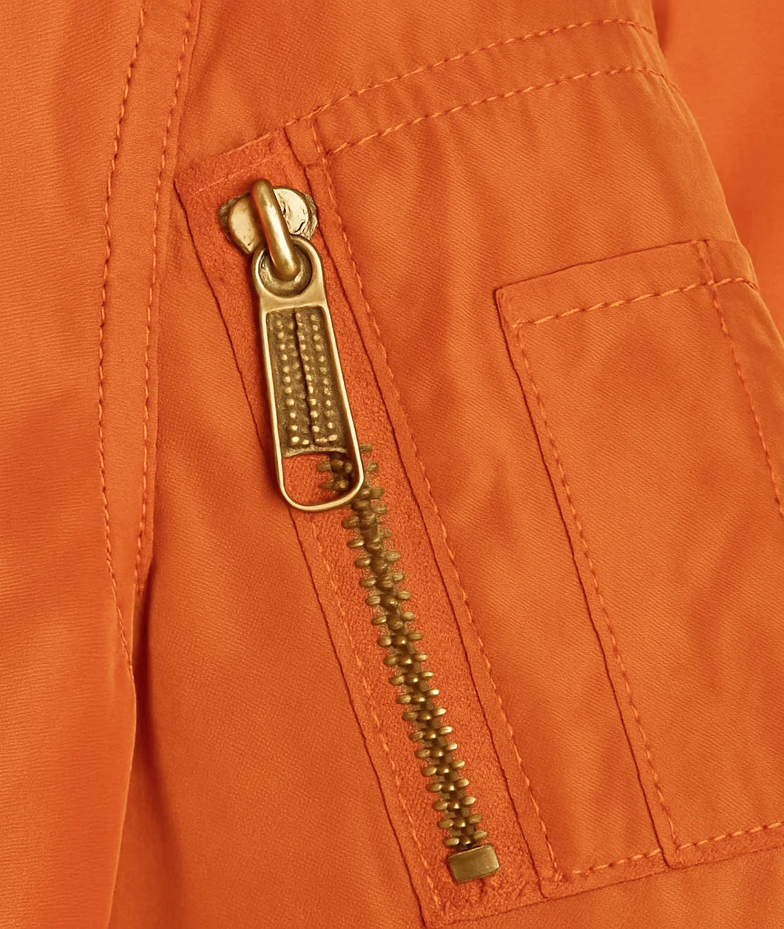 Close-up of a gold zipper on an orange jacket