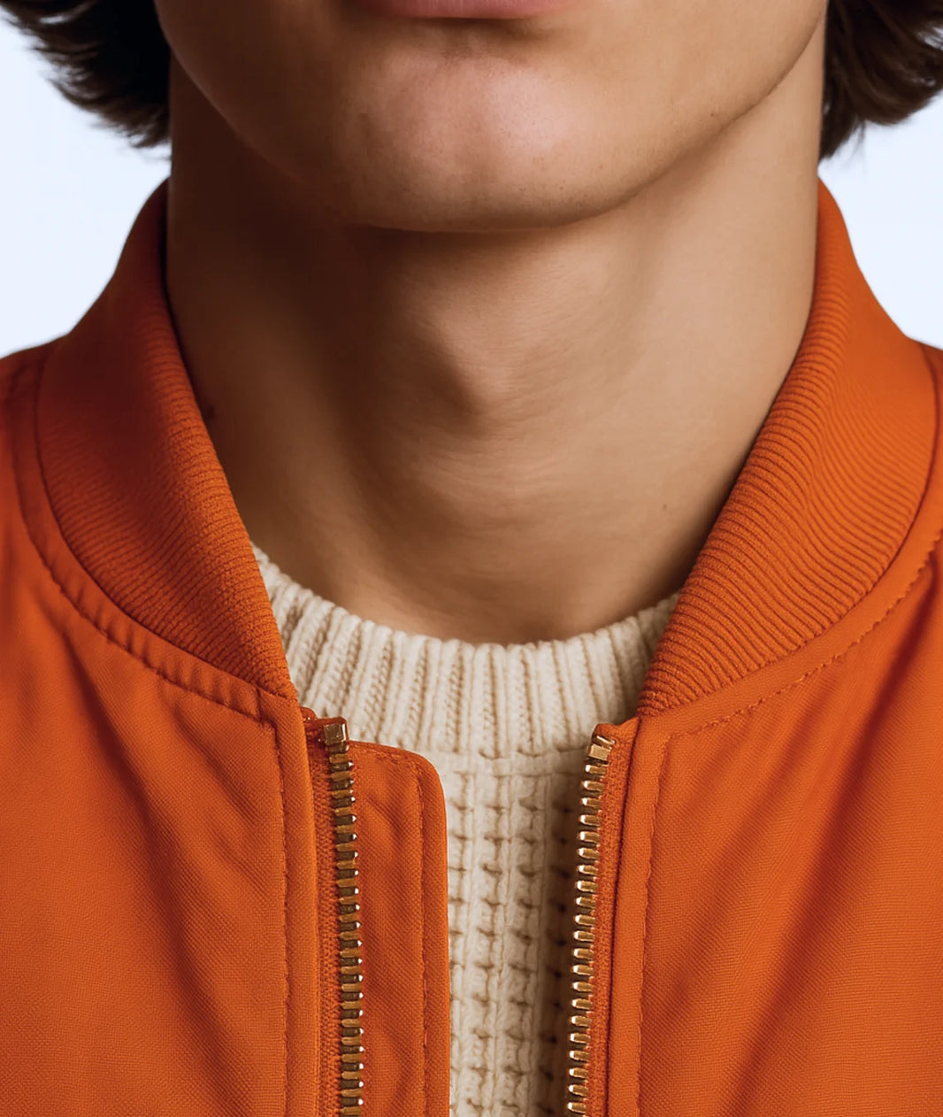 Close-up of a person wearing an orange jacket with a white sweater underneath.