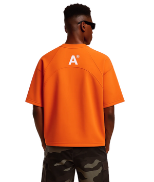 Person wearing an orange shirt with a logo on the back, standing against a white background