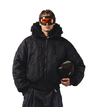 Person wearing a black winter coat and goggles holding a helmet on a white background