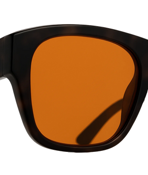 Close-up of oversized square sunglasses with a dark tortoiseshell frame and a warm amber-orange lens, shown against a plain white background.